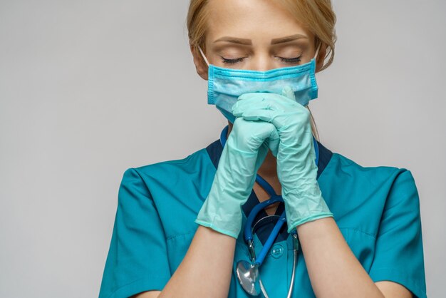 Lekarz pielęgniarki kobieta ubrana w maskę ochronną i rękawice lateksowe - modląc się i mając nadzieję na gest