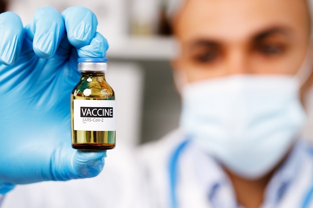 Lekarz płci męskiej trzymający w ręku fiolkę ze szczepionką Sars-cov-2