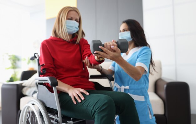 Zdjęcie lekarz pomaga kobiecie na wózku inwalidzkim wykonywać ćwiczenia z hantlami
