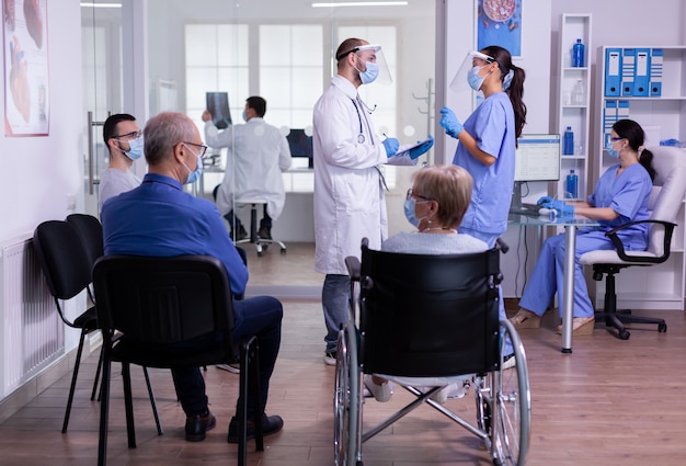 Lekarz rozmawia z pielęgniarką z maskami na twarz trzymając schowek wyjaśniający leczenie stojąc w poczekalni kliniki medycznej przed badaniem pacjenta