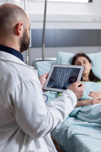 Lekarz Specjalista Monitorujący Chorą Kobietę Wyjaśniający Radiografię Kości Przy Użyciu Komputera Typu Tablet Pracującego Na Oddziale Szpitalnym. Pacjent Odpoczywający W łóżku Wraca Do Zdrowia Po Operacji Chorobowej