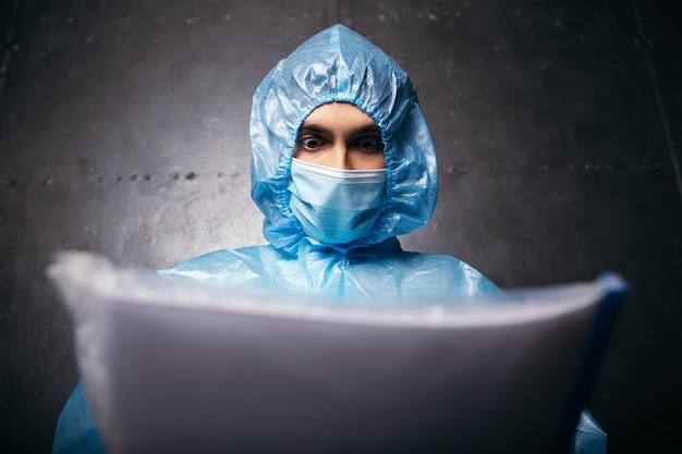 Zdjęcie lekarz stojący przy ścianie nosić kombinezon ochronny, trzymać i czytać dokumenty