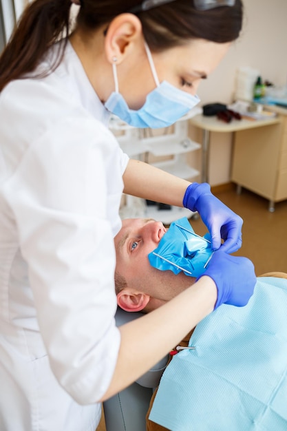 Lekarz stomatolog w trakcie leczenia pacjenta płci męskiej. Kobieta dentysta w maskę z pacjentem siedzącym na fotelu dentystycznym w klinice dentystycznej. Selektywne skupienie