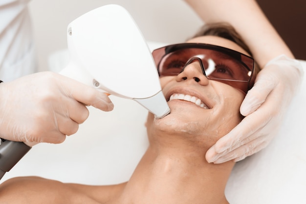 Lekarz traktuje twarz mężczyzny za pomocą nowoczesnego depilatora laserowego