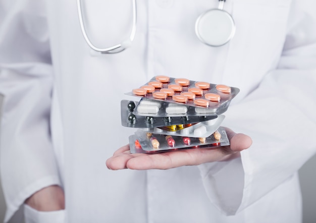 Lekarz trzymając stos różnych tabletek, antybiotyków i tabletek do leczenia wirusów na szarej ścianie szpitala. Makro