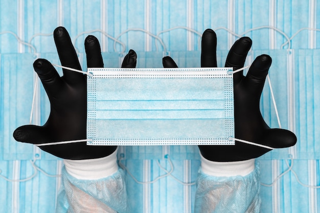 lekarz trzymający niebieską chirurgiczną maskę medyczną w dwóch czarnych rękawicach ochronnych w koncepcji rąk