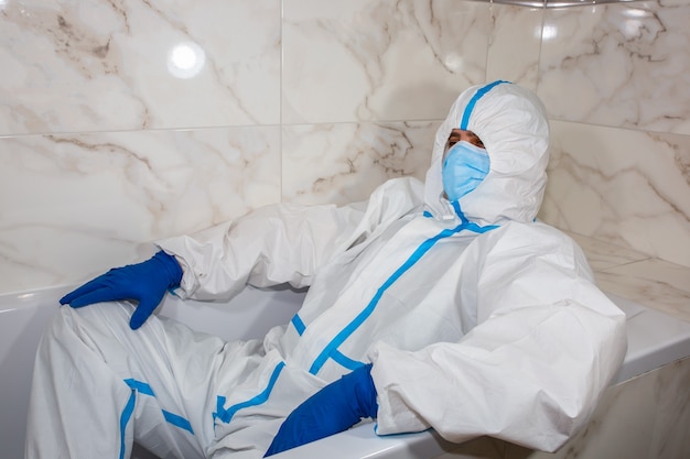 Lekarz ubrany w medyczny strój ochronny, maskę i rękawiczki leżące w wannie. Zrelaksuj się po pracy. Ochrona przed epidemią wirusa. Koronawirus (COVID-19). Pojęcie opieki zdrowotnej.