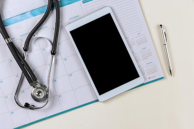 Lekarz w biurze lekarza w kalendarzu ze stetoskopem, tablicą z urządzeniem cyfrowym