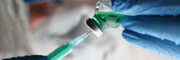 Zdjęcie lekarz w kombinezonie ochronnym i rękawiczkach pobiera lek z fiolki do strzykawki