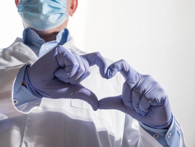 Lekarz w masce i rękawiczkach pokazuje znak serca