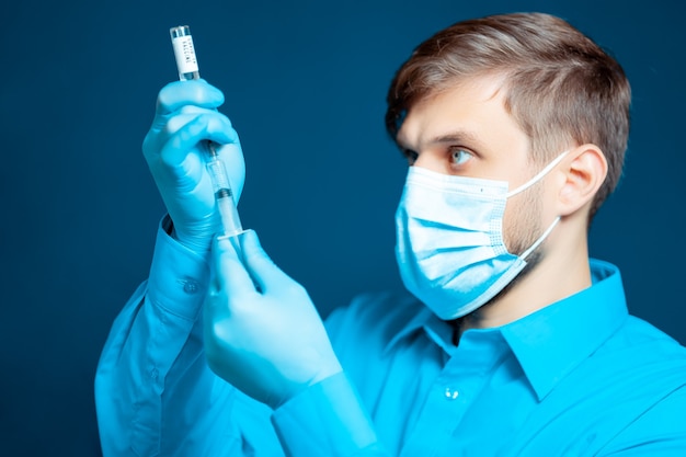 Lekarz w masce medycznej i rękawiczkach, ubrany w niebieski mundur, wybiera szczepionkę do strzykawki