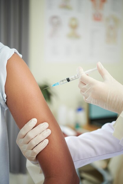 Lekarz w masce podający szczepionkę nastoletniej dziewczynie w klinice profilaktyka szczepień przeciwko zakażeniu koronawirusem