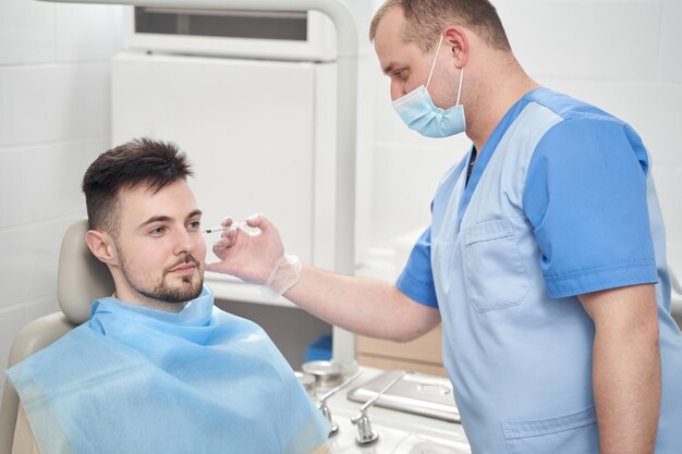 Lekarz w masce robi zastrzyki dla pacjenta płci męskiej