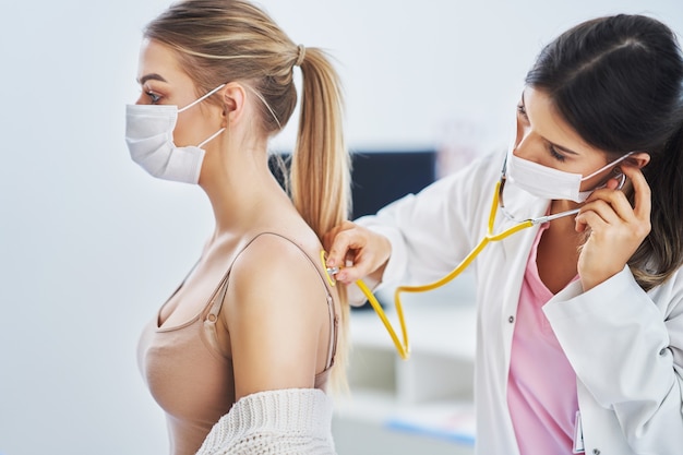 lekarz w masce sprawdzający pacjentkę za pomocą stetoskopu