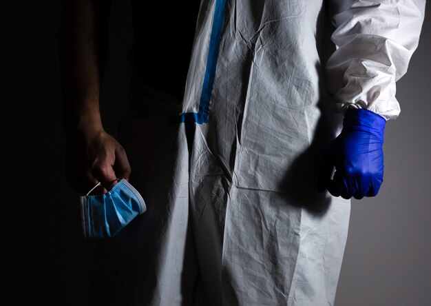 Lekarz w medycznym kombinezonie ochronnym i rękawiczkach, trzymając w ręku maskę. Koniec pandemii wirusów. Ochrona przed epidemią wirusa. Koronawirus (COVID-19). Pojęcie opieki zdrowotnej.