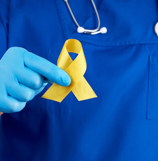 Lekarz w niebieskim mundurze i sterylnych lateksowych rękawiczkach trzyma w dłoni żółtą wstążkę