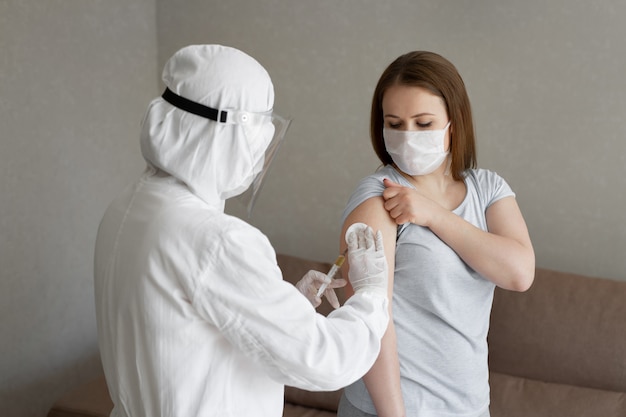 Lekarz w osobistym kombinezonie ochronnym lub zastrzyku PPE zastrzyk szczepionki w celu zwiększenia odporności kobiety chorej na ryzyko zakażenia koronawirusem. Koncepcja koronawirusa, covid-19 i szczepienia