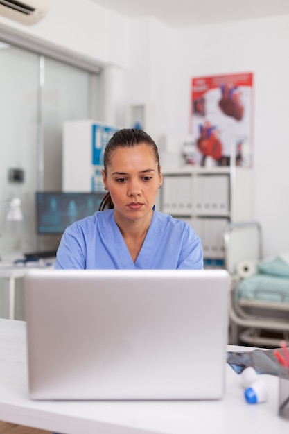 Lekarz wpisuje raport o stanie zdrowia pacjenta na laptopie w gabinecie szpitalnym