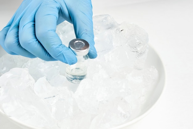 Lekarz wyjmuje fiolkę ze szczepionką z zimnej lodówki i przygotowuje zastrzyk. Fiolki na lodzie. Długotrwałe przechowywanie szczepionki Covid-19. Fiolki ze szczepionką przeciwko koronawirusowi przechowywane w chłodni