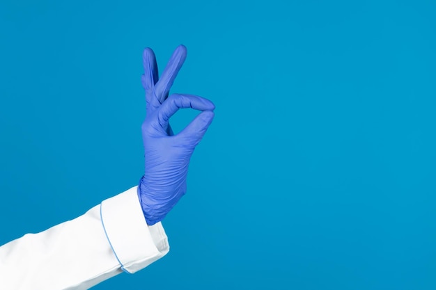 Lekarze ręka w rękawiczce trzyma gestem OK na niebieskim tle z miejscem na kopię