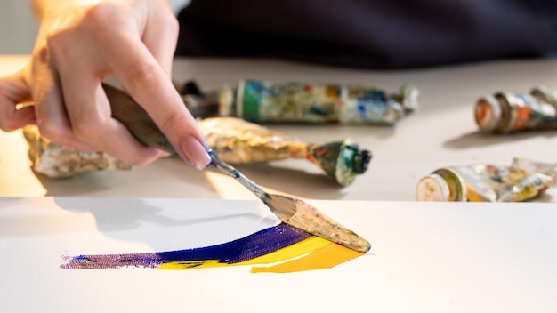 Lekcja malowania Proces twórczy Narzędzia artystyczne Hobby Wypoczynek Nierozpoznawalna kobieta mieszająca niebiesko-żółte kolory farb za pomocą szpachelki na płótnie