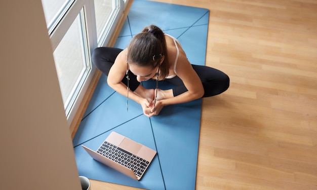 Lekcje jogi online Pozytywna dziewczyna jogi robi poranną praktykę przed laptopem w domu