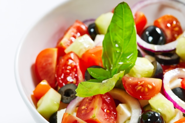 Lekka sałatka grecka ze świeżymi warzywami, przyozdobiona bazylią.