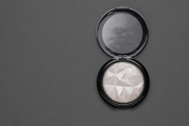 Lekki rozświetlacz w ciemnym słoiczku na szarym tle Minimalna koncepcja makijażu dla kobiet