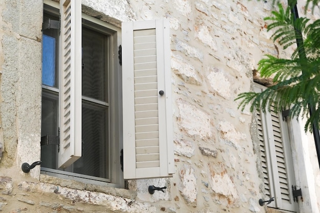 Lekkie okno z okiennicami na ścianie kamieni domowych i betonu