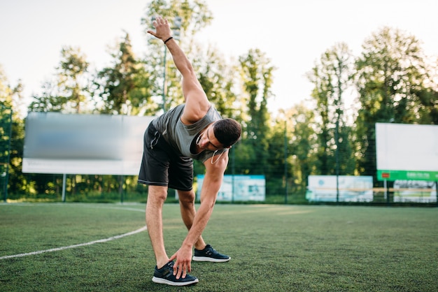 Lekkoatletycznego mężczyzna robi ćwiczenia rozciągające, widok z boku, trening fitness na świeżym powietrzu. Silny sportowiec w parku