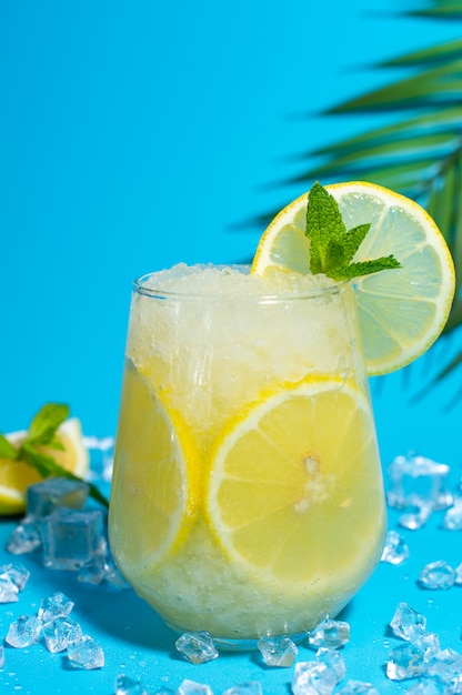 Lemoniada frappe z okrągłym plasterkiem cytryny i mięty na niebieskim lodzie.