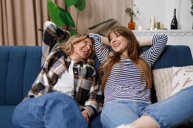 Leniwa matka i córka leżą na kanapie z rękami nad głowami Dwie śmiejące się kobiety w różnym wieku relaksują się na kanapie