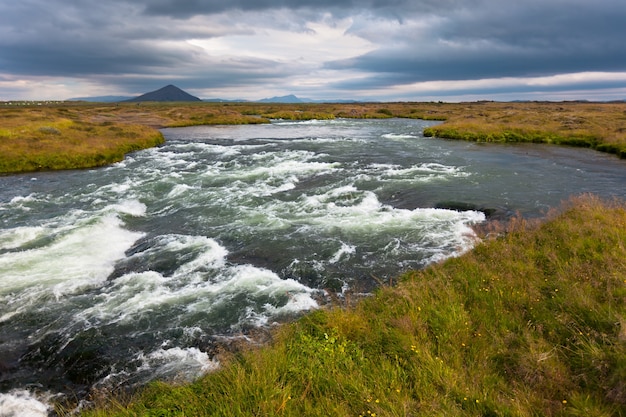 Letni krajobraz Islandii z szalejącą rzeką przy pochmurnej pogodzie