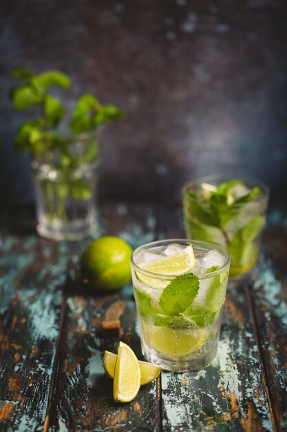 Letni napój Mojito z lodem, brązowym cukrem, plastrami limonki, świeżą miętą w szkle, drewnianym tle rustykalnym, kąt widzenia. Zimny orzeźwiający koktajl idealny na letnią imprezę i zabawę