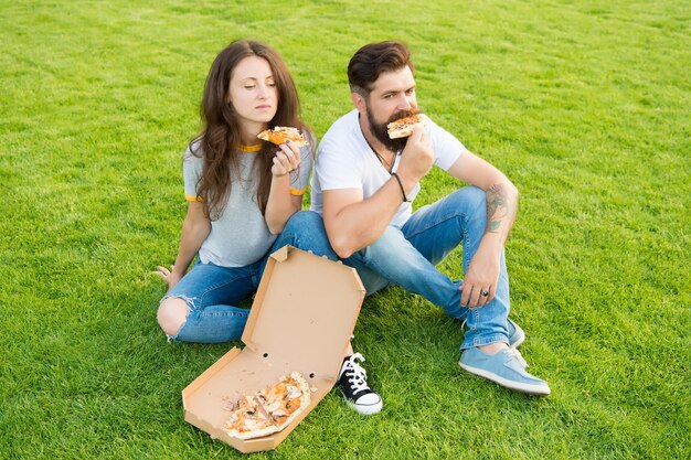 Letni piknik łatwe i szybkie pomysły Fast food Brodaty mężczyzna i kobieta cieszą się tandetną pizzą Zakochana randka na świeżym powietrzu z pizzą Głodni studenci dzielą się jedzeniem Para je pizzę relaks na trawniku