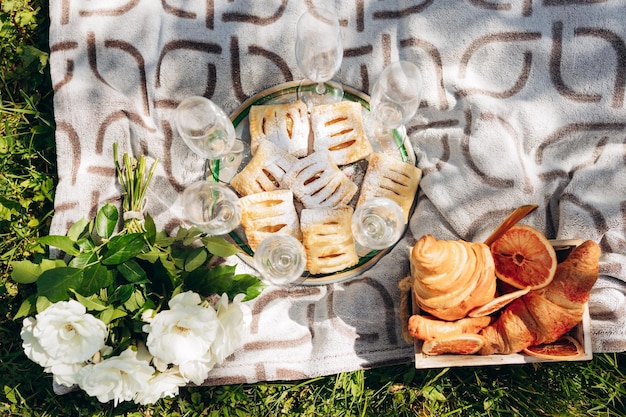 Letni piknik na świeżym powietrzu w słoneczny dzień z rogalikiem, drewnianą deską do krojenia, kieliszkiem do wina i brązowym kocem Rustykalny, przytulny styl