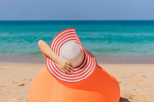 Letni styl życia portret ładna dziewczyna siedzi na pomarańczowej nadmuchiwanej sofie na plaży tropikalnej wyspie, relaksując się i ciesząc się życiem na łóżku powietrznym