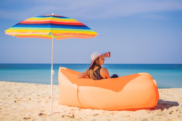 Letni styl życia portret ładna dziewczyna siedzi na pomarańczowej nadmuchiwanej sofie na plaży tropikalnej wyspie, relaksując się i ciesząc się życiem na łóżku powietrznym
