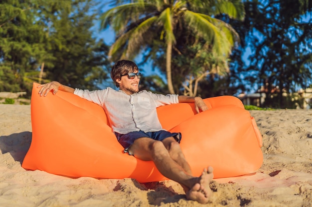 Letni styl życia portret mężczyzny siedzącego na pomarańczowej nadmuchiwanej sofie na plaży na tropikalnej wyspie Relaksujący i cieszący się życiem na łóżku powietrznym