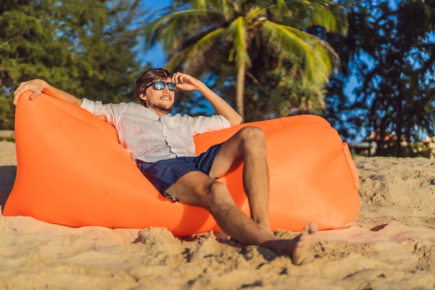 Letni styl życia portret mężczyzny siedzącego na pomarańczowej nadmuchiwanej sofie na plaży na tropikalnej wyspie Relaksujący i cieszący się życiem na łóżku powietrznym