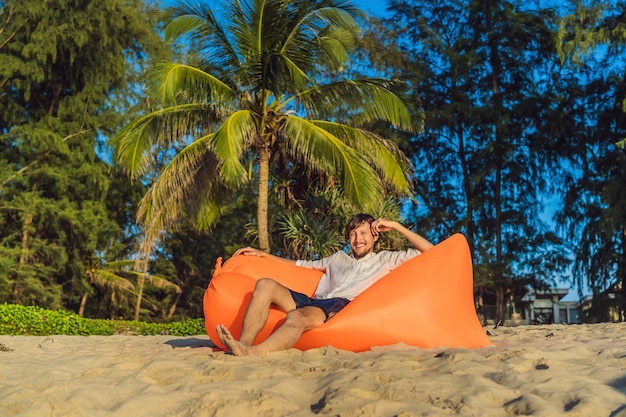 Letni Styl życia Portret Mężczyzny Siedzącego Na Pomarańczowej Nadmuchiwanej Sofie Na Plaży Na Tropikalnej Wyspie Relaksujący I Cieszący Się życiem Na łóżku Powietrznym