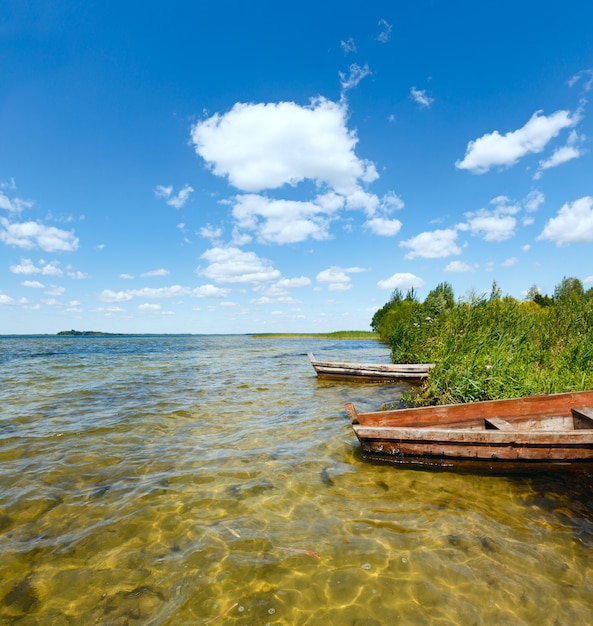 Letni widok na jezioro z drewnianymi łodziami w pobliżu brzegu.