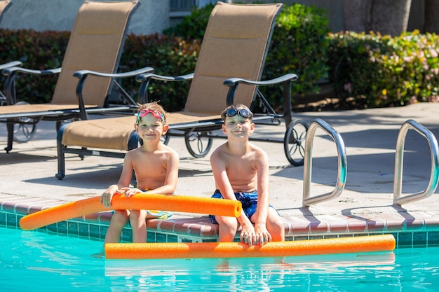 Zdjęcie letnia aktywność na świeżym powietrzu koncepcja zabawy zdrowia i wakacji bracia chłopcy w wieku ośmiu i pięciu lat w okularach do pływania z makaronem siedzą przy basenie w gorący letni dzień