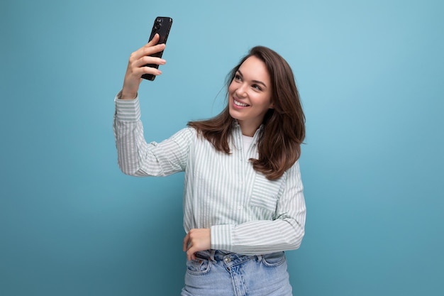 letnia brunetka kobieta używa smartfona w dłoni na niebieskim tle z miejsca na kopię