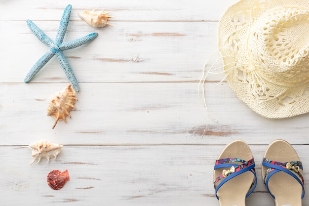 Zdjęcie letnia koncepcja tła kobiece sandały, rozgwiazdy, muszle, słomkowy kapelusz na jasnej drewnianej powierzchni
