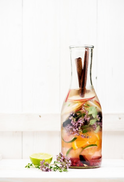 Letnia lemoniada z jagodami, ziołami i owocami w szklanej butelce na białym drewnianym tle