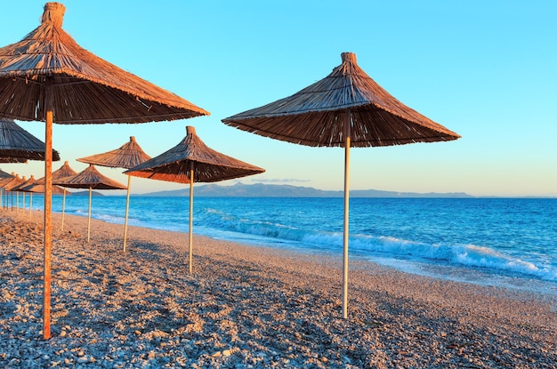 Letnia plaża o zachodzie słońca ze słomianymi parasolami (Albania).