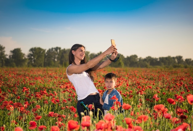 Letnia scena szczęśliwej matki i syna biorących selfie ze smartfonem na polu makowym. Letni słoneczny dzień