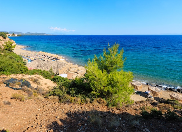 Letnia sceneria morza z przejrzystą wodą i piaszczystą plażą. Widok z brzegu (Sithonia, Halkidiki, Grecja). Ludzie są nie do poznania.