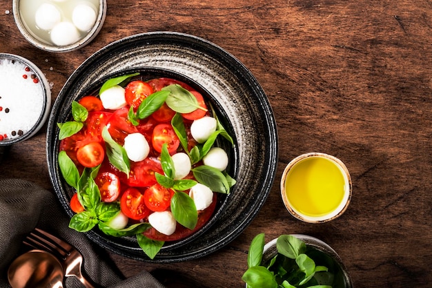 Letnia włoska sałatka Caprese z czerwonymi pomidorami i serem mozzarella z zielonymi liśćmi bazylii i dressingiem z oliwy z oliwek Drewniany stół z widokiem z góry